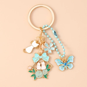Dettaglio di portachiavi dorato con fiori blu, gatti bianchi e ciondolo a farfalla