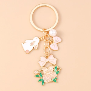 Détail d'un porte-clés doré avec lapin en émail blanc, fleurs roses et une perle