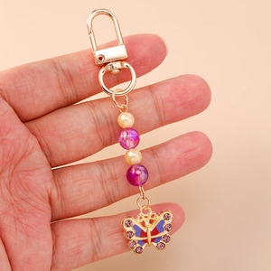 Kleurrijke vlinder sleutelhanger met paarse strass en parels vastgehouden tegen beige decor