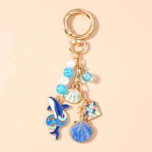 Détail d'un porte-clés nautique avec baleine en émail bleu, breloques coquillages et métal doré