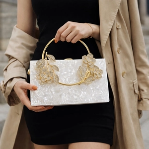 Detail of white acrylic clutch bag featuring crystal floral gold ring handle and marble texture