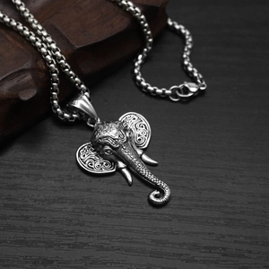 Vintage stainless steel elephant head pendant with tribal patterns on a dark wood background