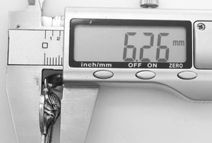 Macro shot of an elephant pendant thickness being measured at 6.26 mm with a digital caliper