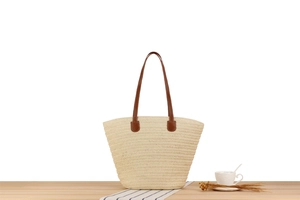 Close-up of paper straw woven tote bag with premium brown leather straps on a wooden table