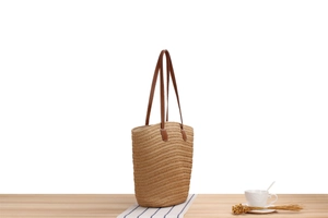 Detailed close-up of woven paper straw texture and brown leather strap on a shoulder bag