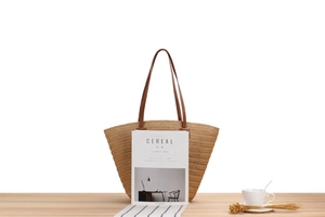 Detail of woven straw tote bag featuring brown leather straps and hand-stitched details