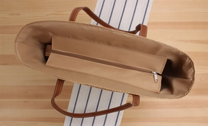 Top view of woven tote interior with a zippered pocket and brown leather handles