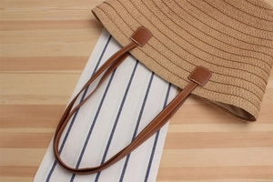 Macro detail of natural straw tote bag with horizontal weave and leather shoulder straps