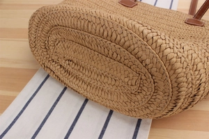 Detailed close-up of woven paper rope beach bag with reinforced oval base and leather straps