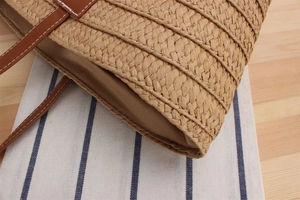 Close-up of woven paper straw bag with brown leather handles and fine white stitching