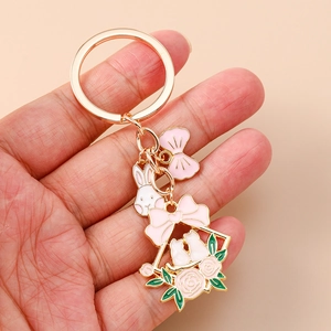 Detail of a golden bunny keychain with pink bows and floral cat charm in hand