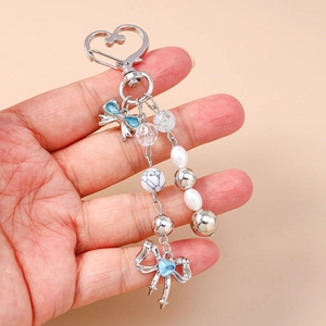 Detail of beaded keychain with silver heart clasp, pearl beads, and blue gemstone bow charm