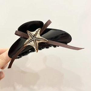Détail d'une pince à cheveux en acétate noir avec ruban brun et breloque étoile de mer