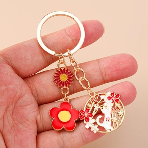 Detail of a floral cat keychain with enamel finish and golden metal ring and charms