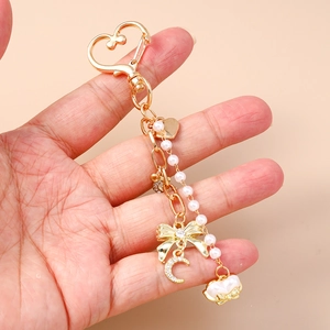 Golden heart keychain with diamond bow and pearl charms held in hand on pink background