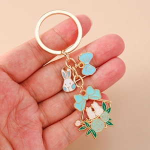 Detailed close-up of a golden flower bunny keychain with blue enamel bow held in hand