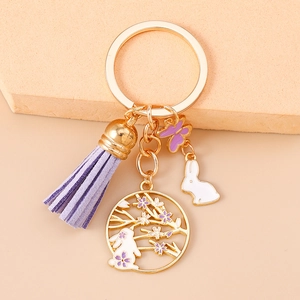 Detail of golden keychain with purple tassel, rabbit charm and floral cutout pendant