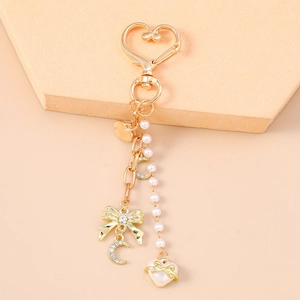 Close-up of golden bow keychain with heart clasp, pearls, and moon pendant