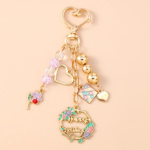 Detail of golden heart keychain with purple beads and Happy Holidays floral wreath charm