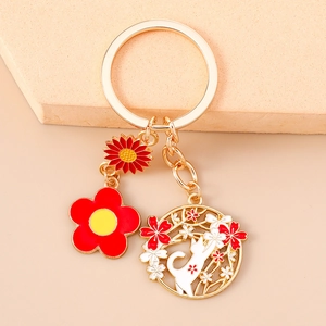 Detail of gold metal keychain with red enamel flowers and a white cherry blossom cat charm