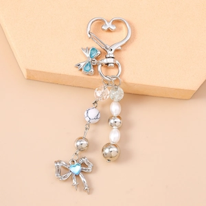 Close-up of silver heart-shaped keychain with blue bow, pearls, and star bead details