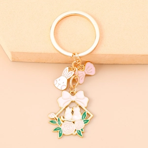Detailed view of gold flower rabbit keychain with enamel charms on peach background