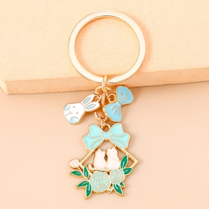 Detail shot of a light gold floral rabbit keychain with blue bow and cat charm pendants