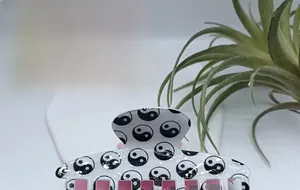 Detailed view of white hair claw clip with classic Tai Chi pattern and pink comb teeth