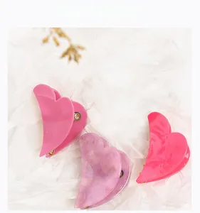 Close-up of three acetate heart hair claws in pink and purple marble on white paper