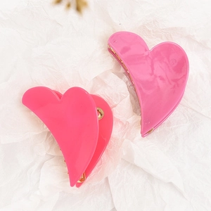 Pair of glossy bright pink heart-shaped acetate hair claws on a white textured background