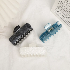 Three elegant large acrylic hair claws in marble and blue on a soft white fabric background