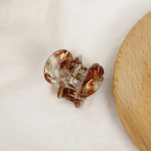 Mini acetate hair claw clip with amber tortoise shell pattern and metal spring on white fabric