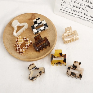 Set of 7 acetate checkered hair claws with marble and leopard patterns on a rustic wooden tray