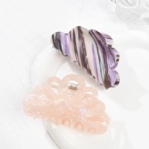 Elegant marble pattern and peach pink cutout acrylic hair claws displayed on a white plate