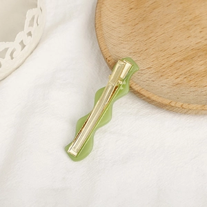 Light green wavy acetate hair clip with gold metal duckbill grip on white fabric