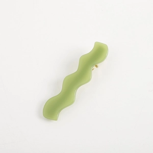 Macro view of light green wavy acetate hair clip with a polished gold metal fastener