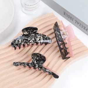 Détail de pinces à cheveux en acétate avec marbre noir et intérieur rose sur bois