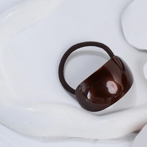 Close-up of brown elastic hair tie with oval acetate detail and gold lettering
