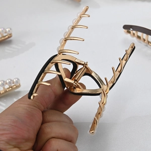 Détail d'une pince à cheveux dorée avec perles blanches et ressort métallique robuste