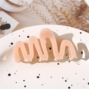 Elegant wave-shaped acetate hair claw in soft pink with a gold metal spring mechanism