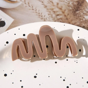 Elegant brown wave-shaped acetate hair claw clip on a stylish ceramic plate background