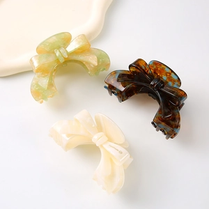 Three elegant acetate bow hair claws in marble green, classic tortoiseshell, and cream white