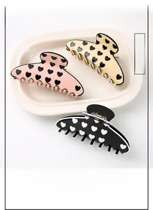 Trois grandes pinces à cheveux à motif cœurs en rose, beige et noir sur plateau céramique