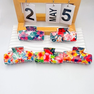Five large floral hair claws with tropical patterns on a white wavy display stand