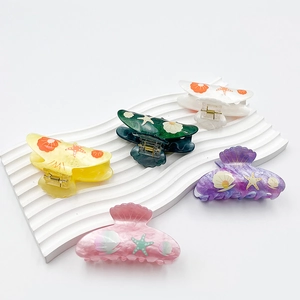 Marine shell and starfish acrylic hair claws in assorted colors on a wavy white display