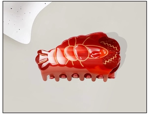 Detailed macro view of a glossy red lobster hair claw clip with golden accent lines