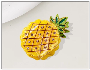 Detail of yellow acetate pineapple hair claw clip with pink rhinestones and green leaves