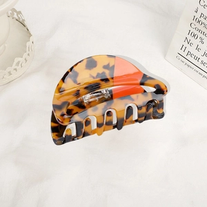 Fashionable acetate hair claw clip with tortoiseshell and orange splicing on white fabric