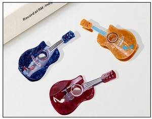 Close-up of guitar-shaped acetate hair claws with marble texture and sparkling rhinestones