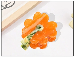 Close-up of orange floral acetate hair claw with marble texture and green rhinestone